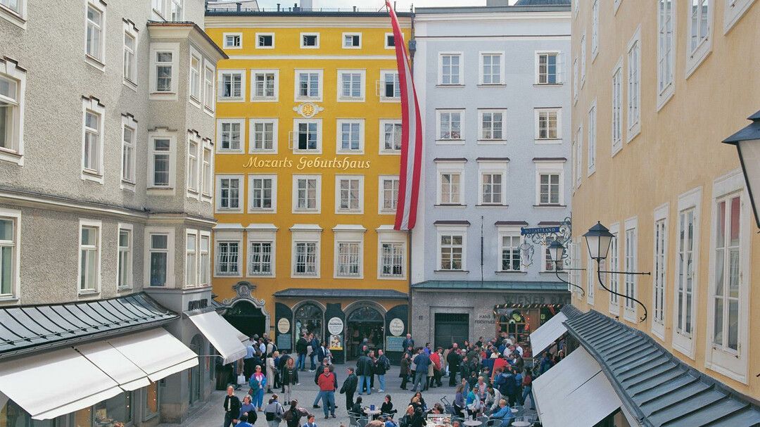 Yellow stone building (Mozart's birthplace) surrounded by pastel-colored stone buildings.