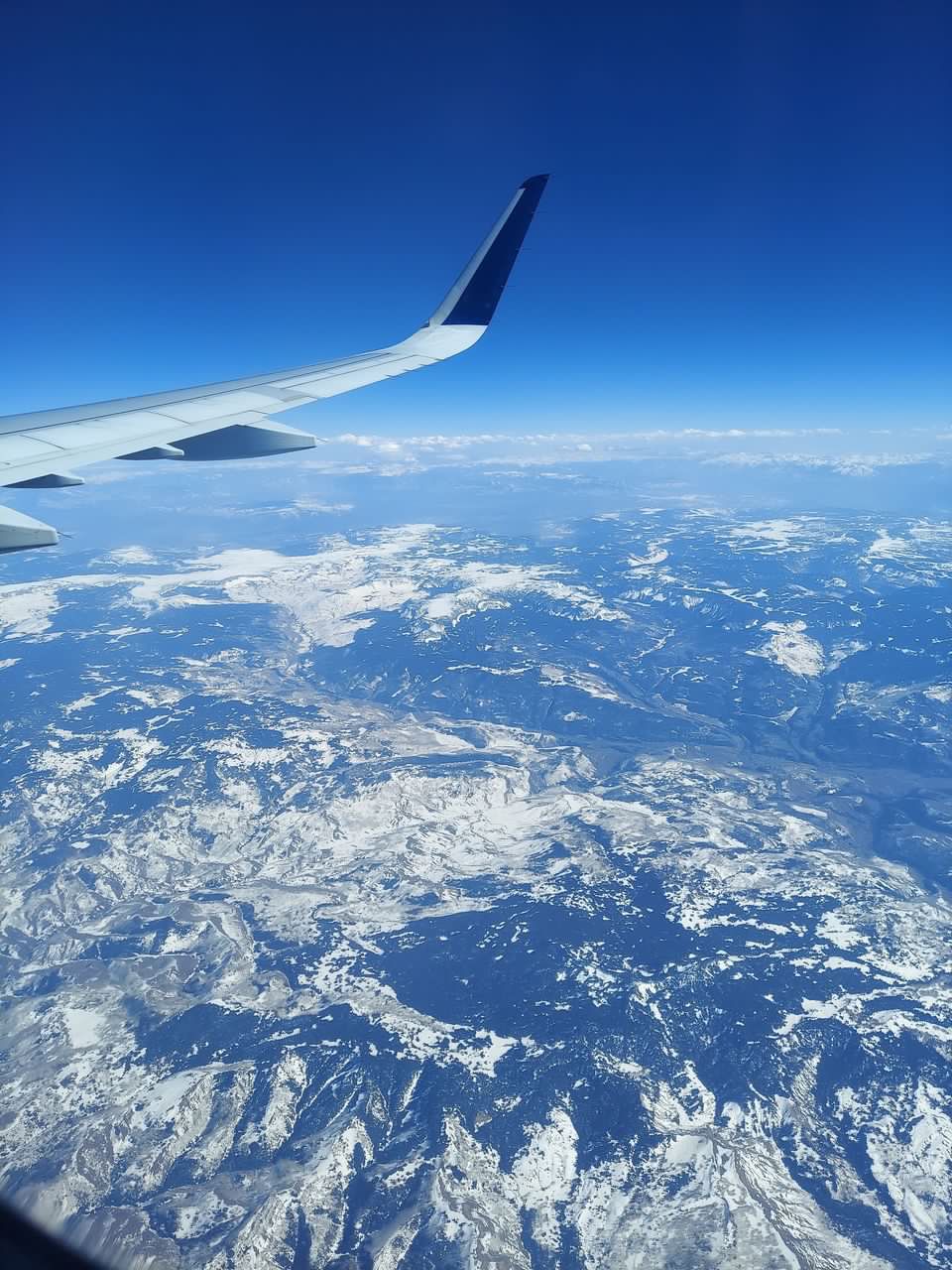 View of snow-capped mountains from an airplane, with the wing of the plane visible.