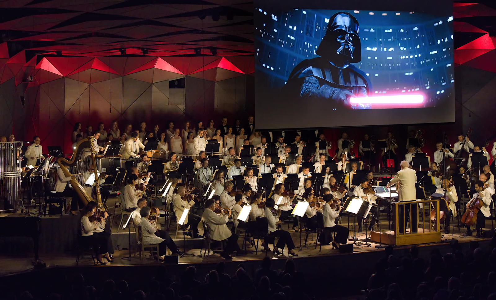 An orchestra plays underneath a large screen showing scenes of Star Wars movies.