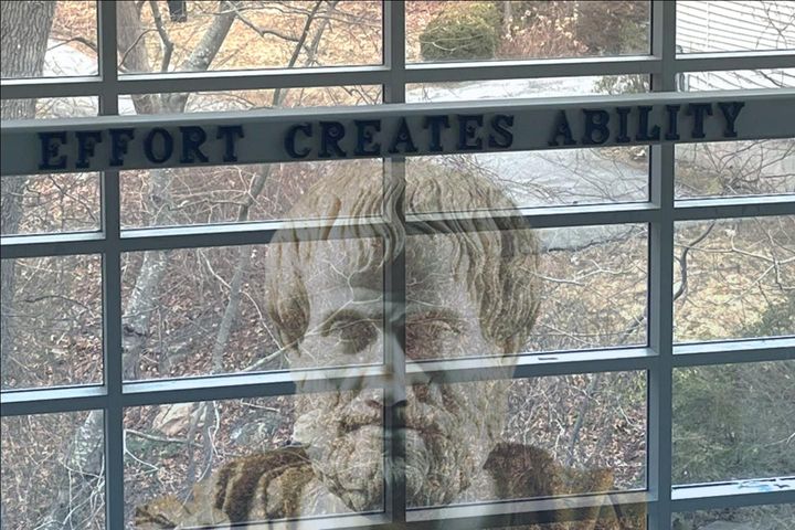 A bust of Aristotle superimposed on the sign that says "Effort Creates Ability."