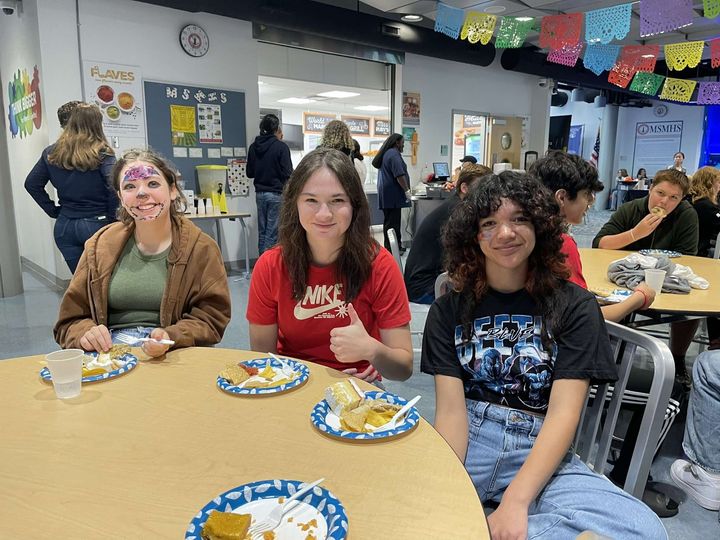 Students sit around a table with plates of traditional Hispanic food.